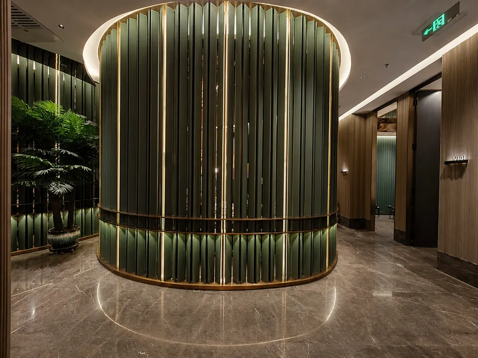 Curved green vertical-fin metal screen defining a private hospitality zone beside the circulation path