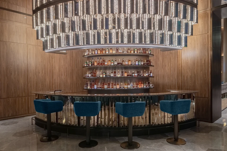 Completed hotel bar with a curved counter, four blue stools, bottle display and suspended feature installation.