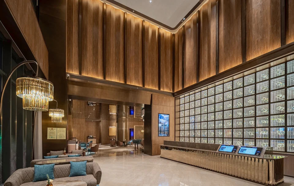 Completed double-height lobby corner showing the illuminated glass-block wall, reception counter and warm wall panels.