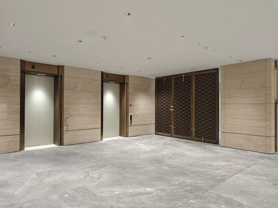Completed lift lobby with bronze-toned surrounds and a patterned metal screen at Guangdong Olympic Sports Center.