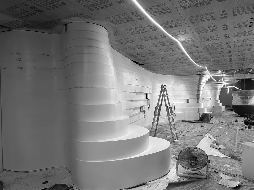 On-site installation view of a layered curved enclosure with a ladder, protective covering and temporary equipment at Yunan Office Building, Guangzhou.