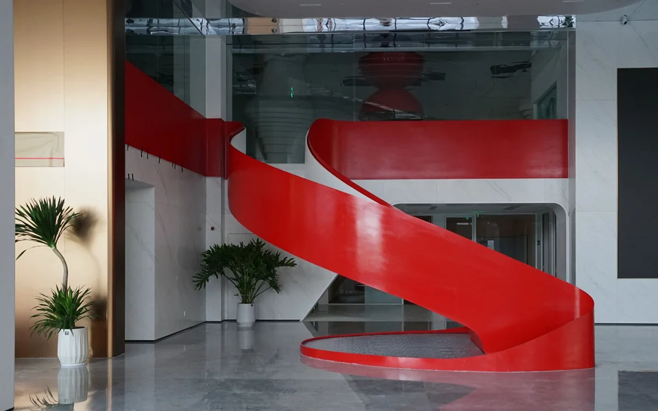 Completed lobby interior centred on the full curve of a red sculptural stair at Yunan Office Building, Guangzhou.