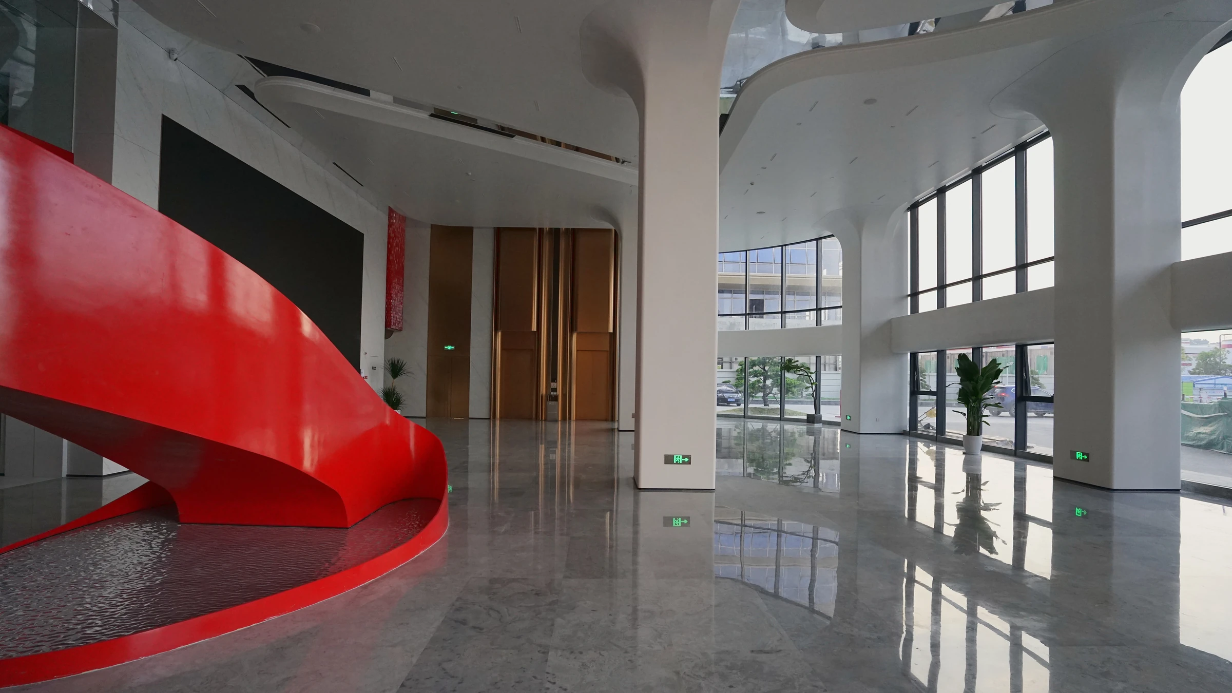 Completed lobby overview with a red sculptural stair, bronze lift portals and a white curved enclosure at Yunan Office Building, Guangzhou.