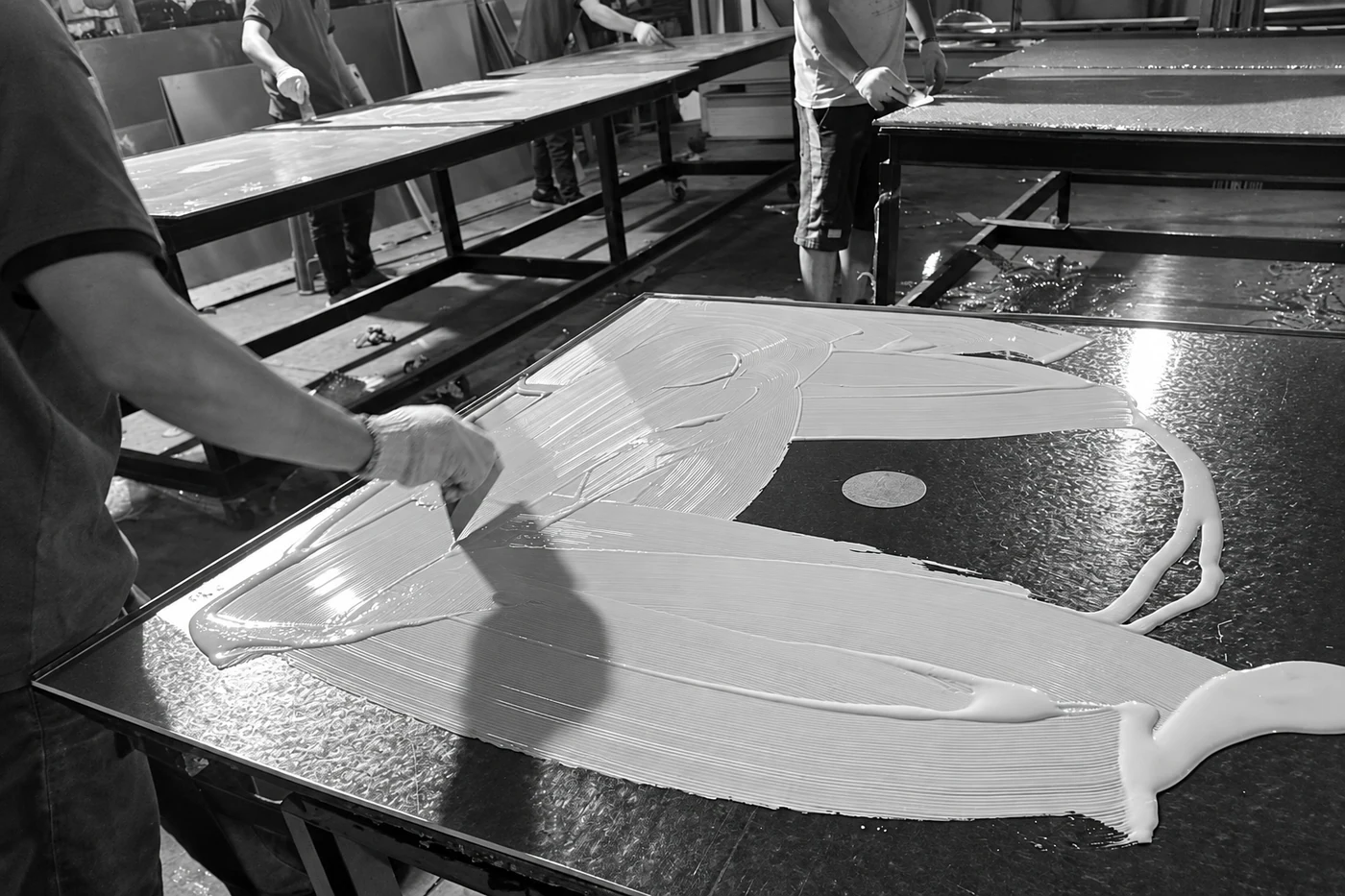 Workers spreading adhesive across metal sheets in the workshop.