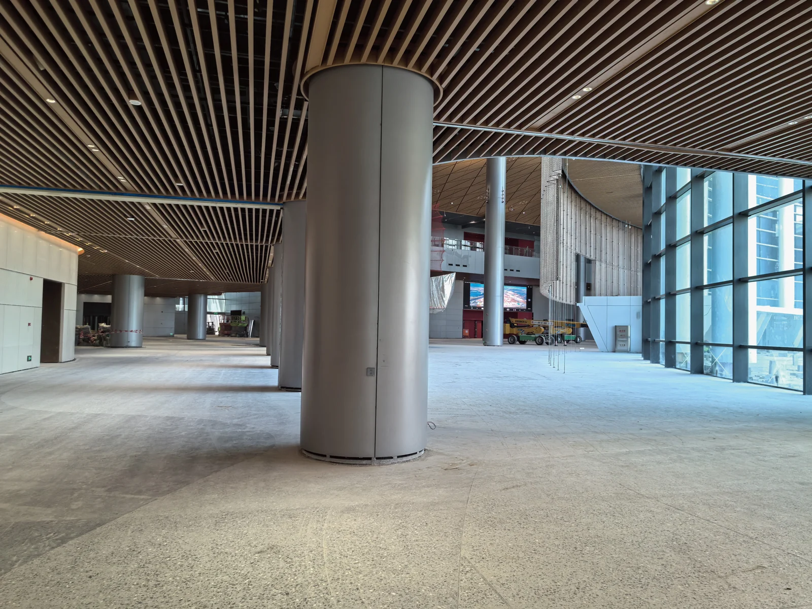 Aluminum baffles surrounding round columns in an open hall under construction.