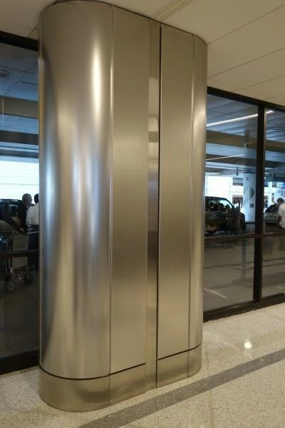 Silver column cladding with a wide flat face, curved corners, vertical interfaces and a horizontal base detail