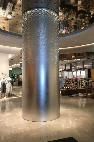 Round column in a retail interior with dense upper perforations transitioning into an unperforated lower surface