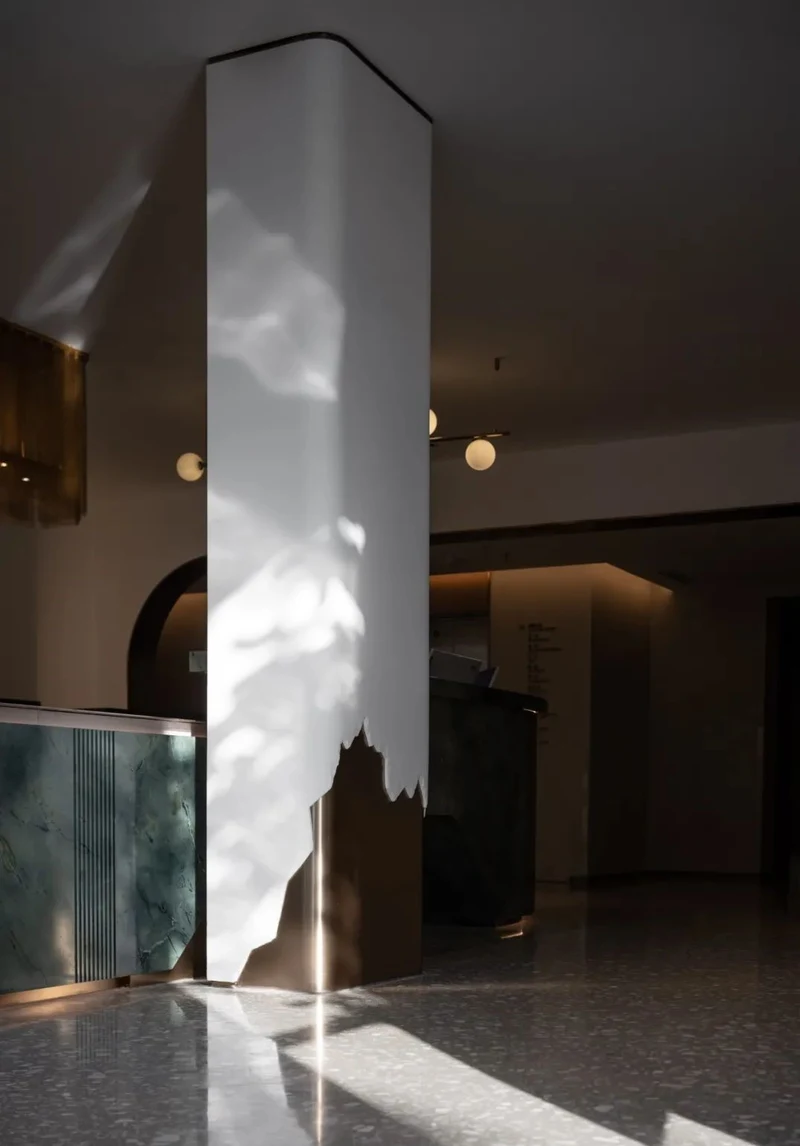 Champagne-tone metal partially wraps the base of a white square column with an irregular upper edge