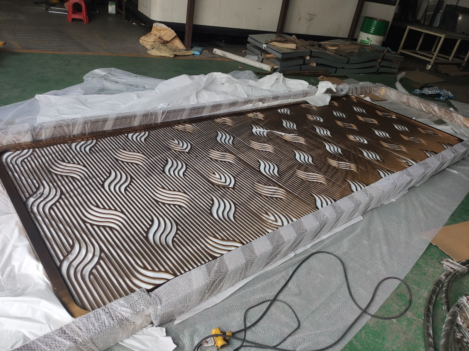 Finished bronze-tone cut-pattern screen panel protected for delivery in the workshop